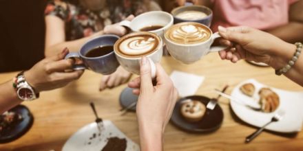gruppe von leuten stößt mit kaffeetassen an latte art