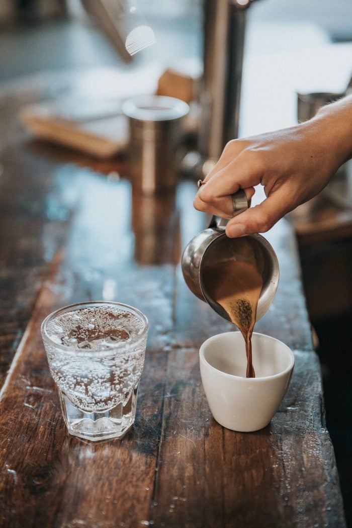 Barista-gießt-Kaffee-in-Tasse-Wasserglas mit der richtigen Kaffeedosierung