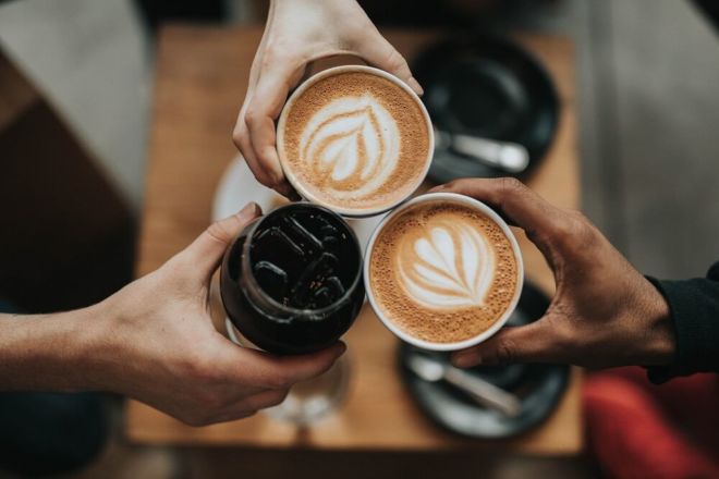 Drei Personen stoßen mit Kaffee an