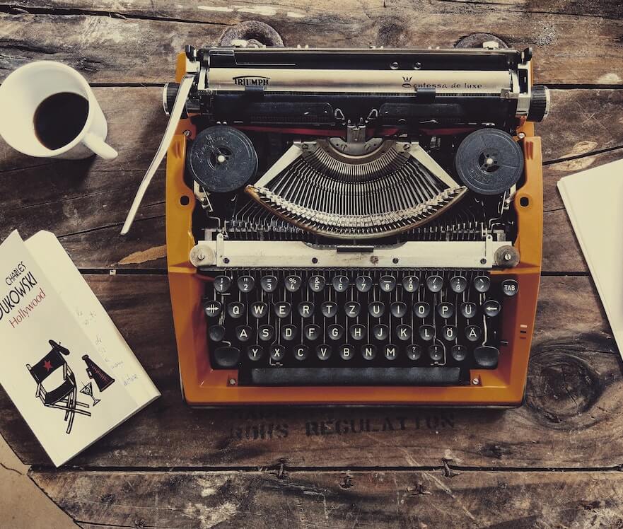 Alte Schreibmaschine mit Kaffee und Buch auf Schreibtisch