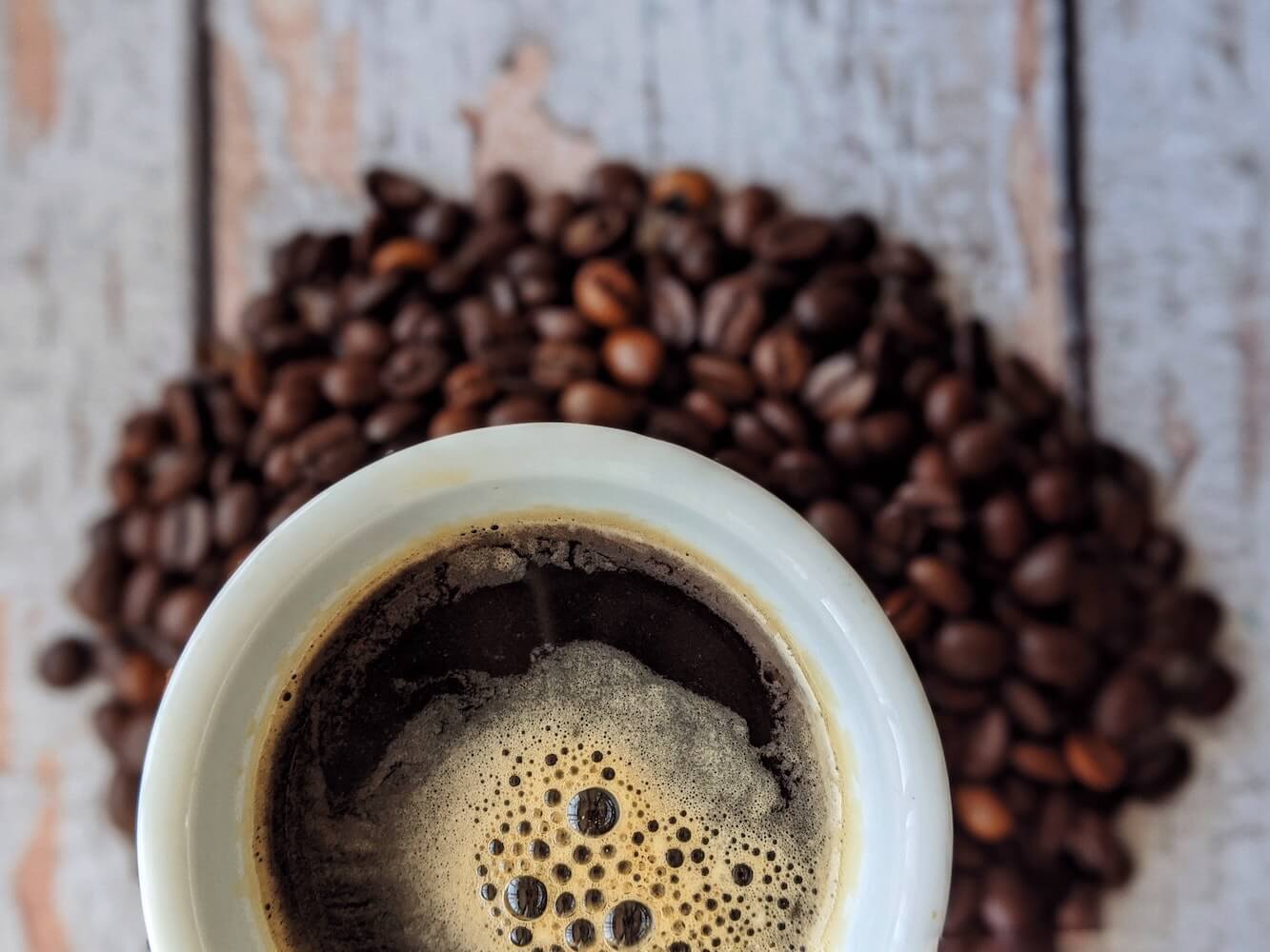 frischer Kaffee in Tasse mit Kaffeebohnen auf Tisch